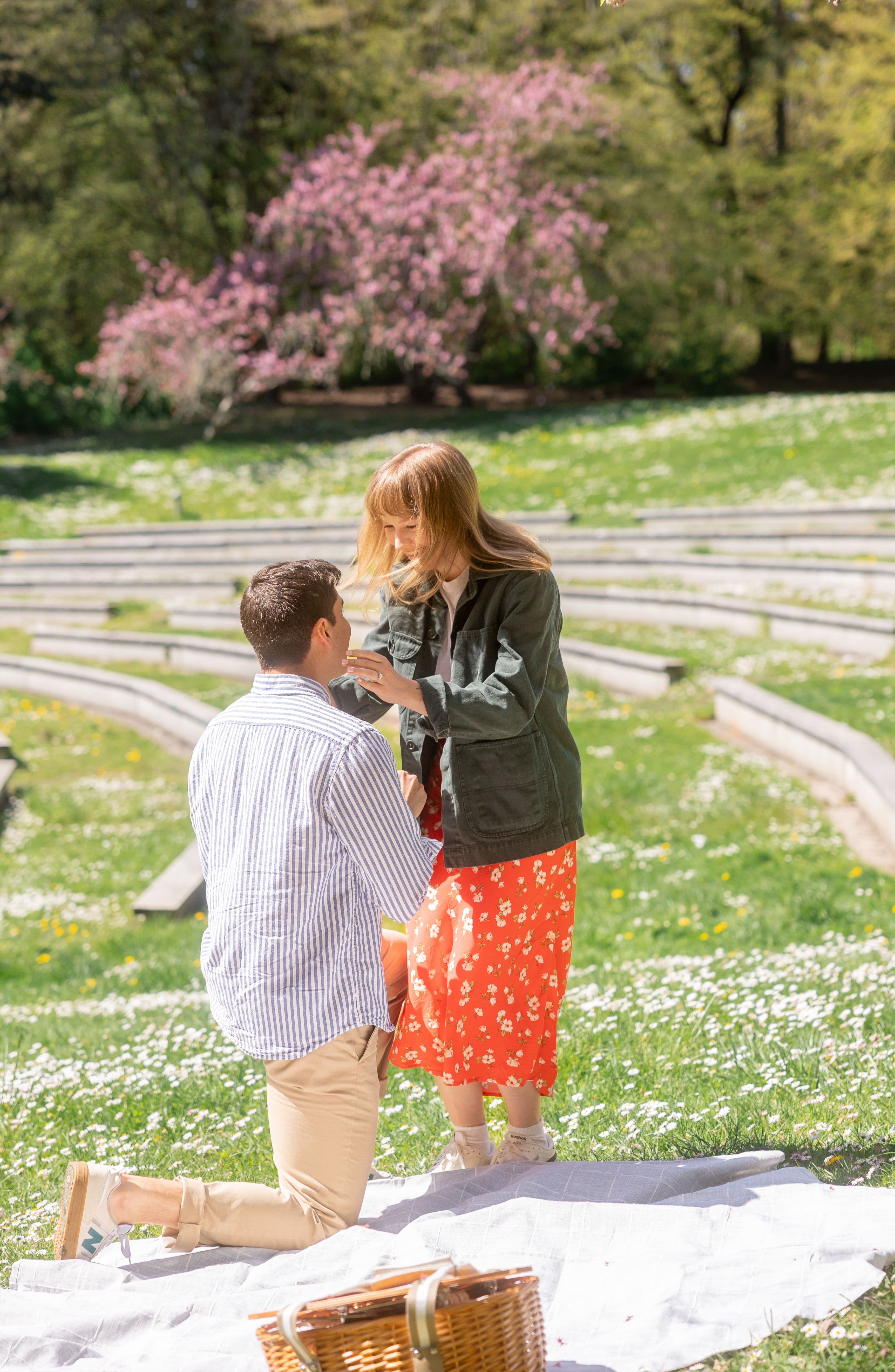 Man down on one knee proposing to his fiance at a park on a sunny day